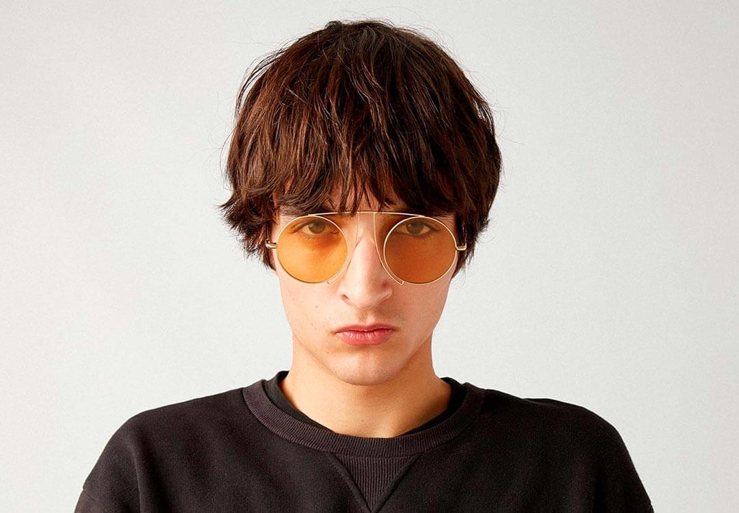 Male model with messy hair over his forehead, wearing designer glasses by Kaleos in an aviator style.