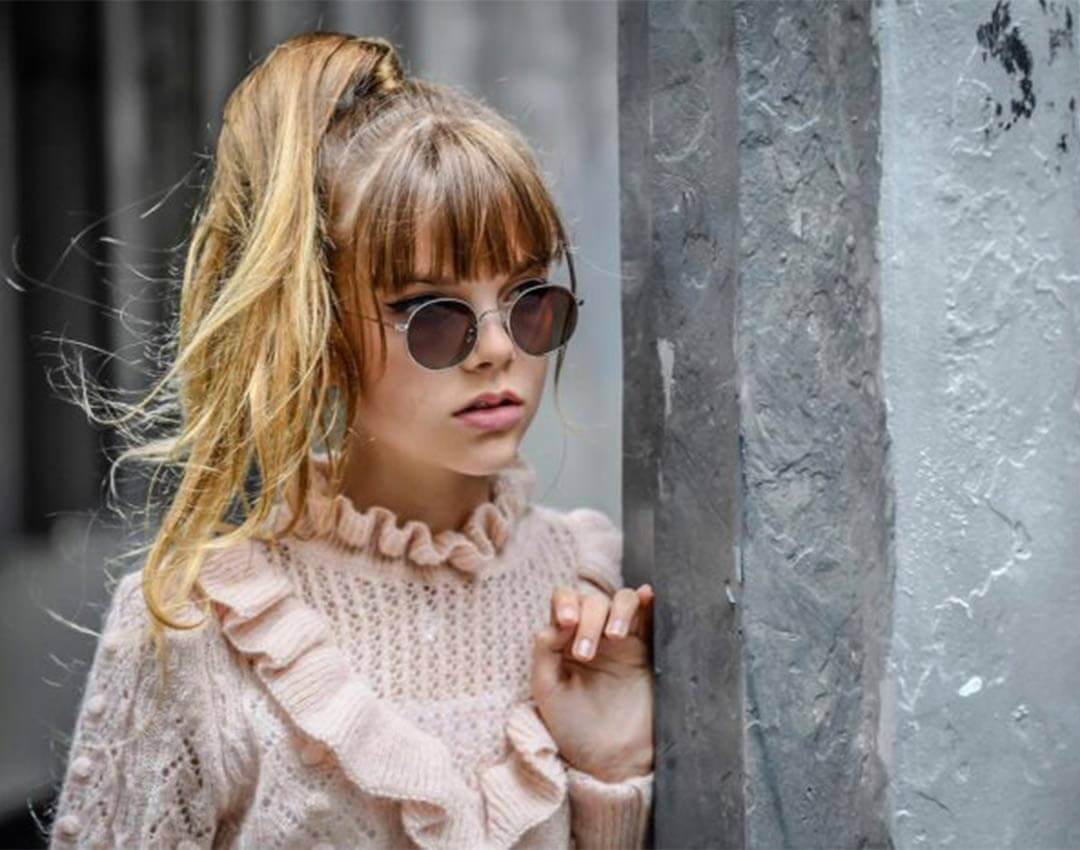A young girl wearing a pink top and designer sunglasses by Nathalie Blanc.