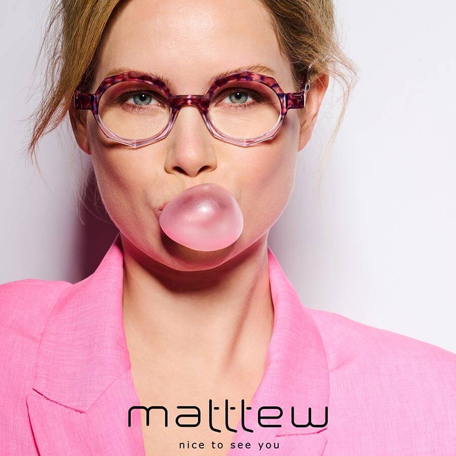 Woman in pink blazer chewing pink bubble gum, wearing pink-framed tortoiseshell glasses from Matttew eyewear.