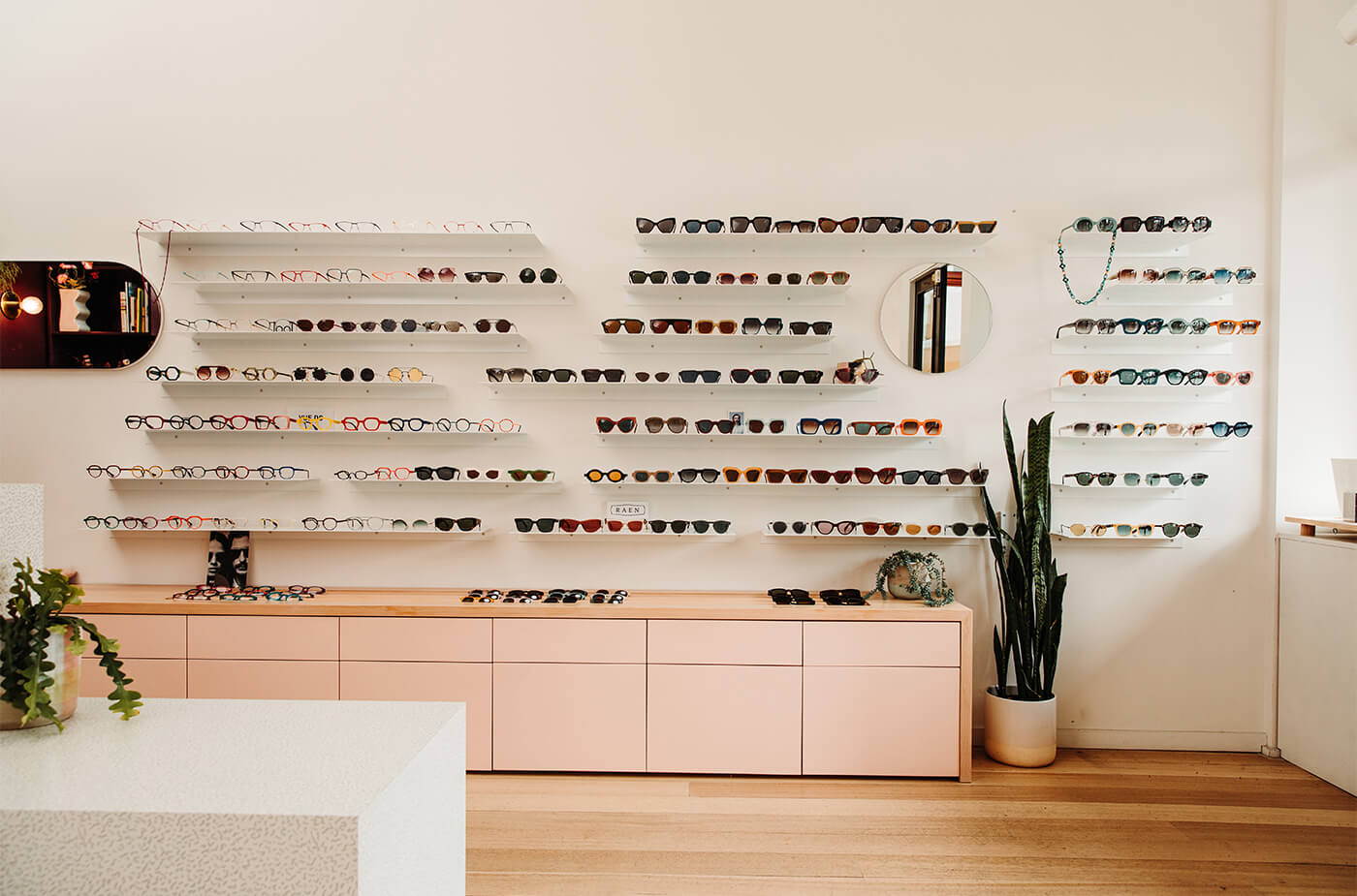 Designer glasses and eyewear displayed on glass shelves on a wall in an independent store.