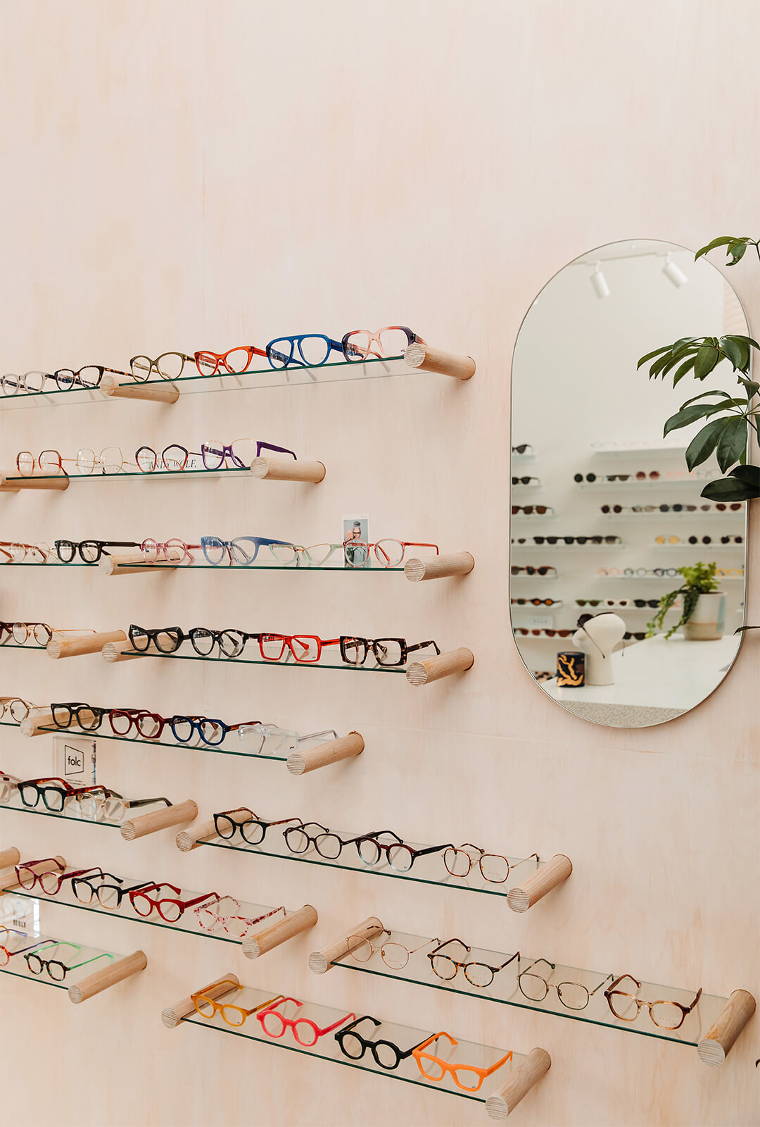 Designer glasses on glass shelves next to a mirror in a boutique eyewear store.
