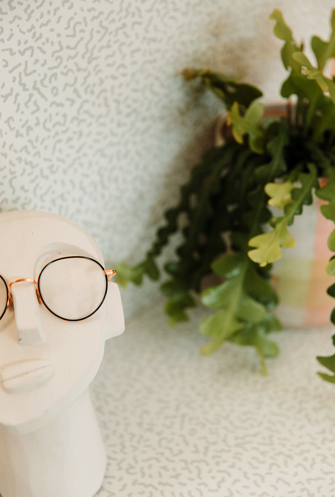 A pair of kids glasses placed on a modern mannequin head next to a plant in an eyewear store.